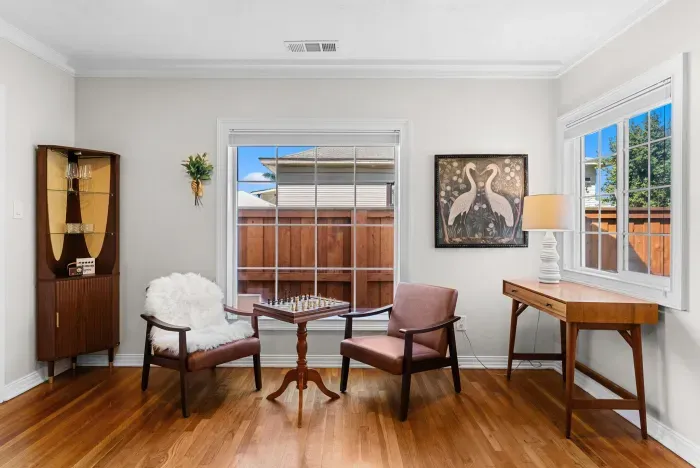 Sunlit mid-century lounge with chess set, writing desk, and hardwood floors