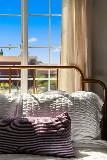 Sunlit bedroom with brass bed, crisp white linens, and blue-sky views.