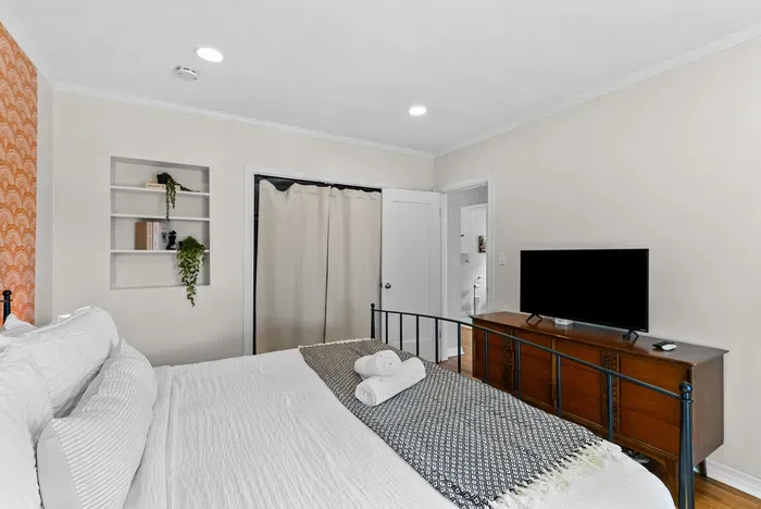 Bright bedroom with crisp linens, TV, built-ins, and cozy accent wall.