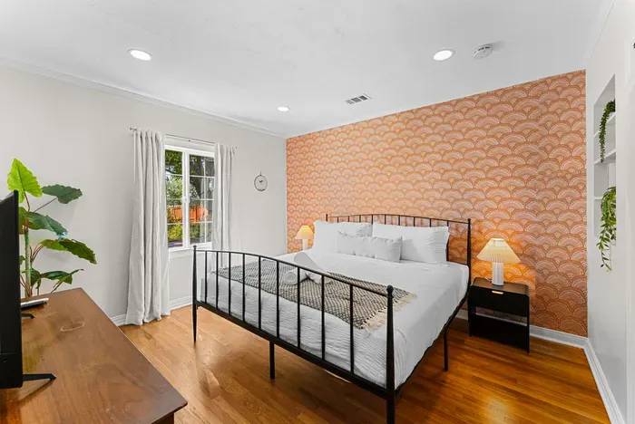Bright bedroom with chic accent wall, hardwoods, and TV