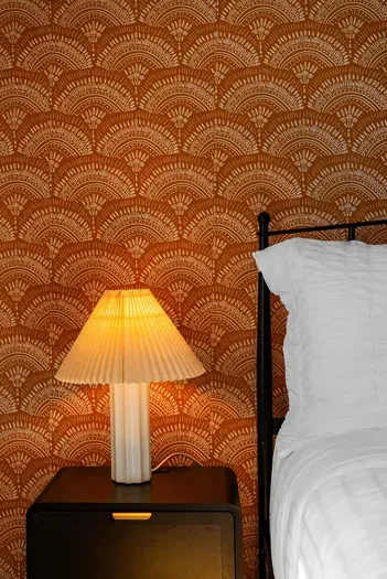 Cozy bedside with Art Deco wallpaper, warm lamp, and crisp white linens.