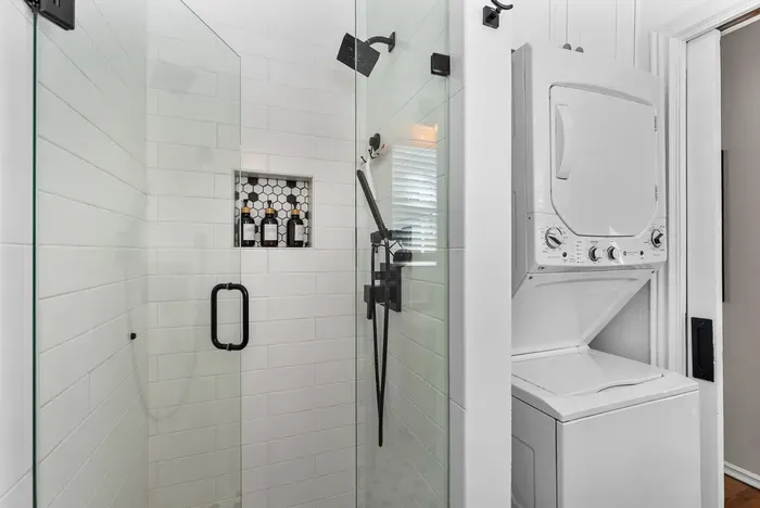 Modern glass shower with black fixtures and convenient in-unit laundry.