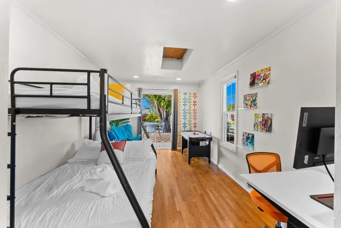 Sunny bunk room with workspace, arcade game, and patio with tropical view